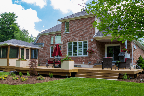 A photo of a newer two-story brick home. There is a new wooden deck, gazebo, and garden designed and built by Kerr & Kerr Landscaping. The lawn is green and cut.