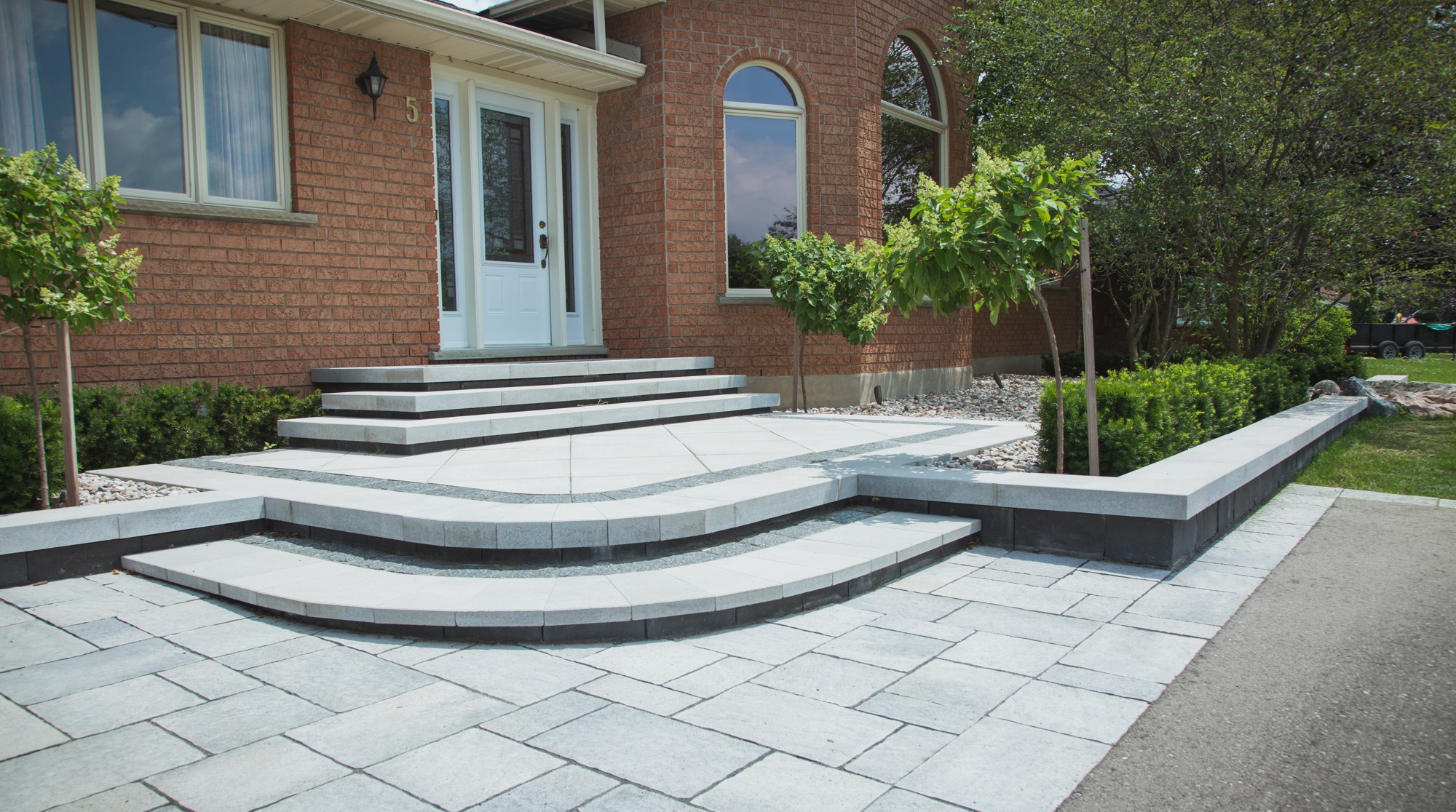 This image shows a brick house with a white door, large windows, and a landscaped front yard featuring a multi-level, curved stone walkway and steps.