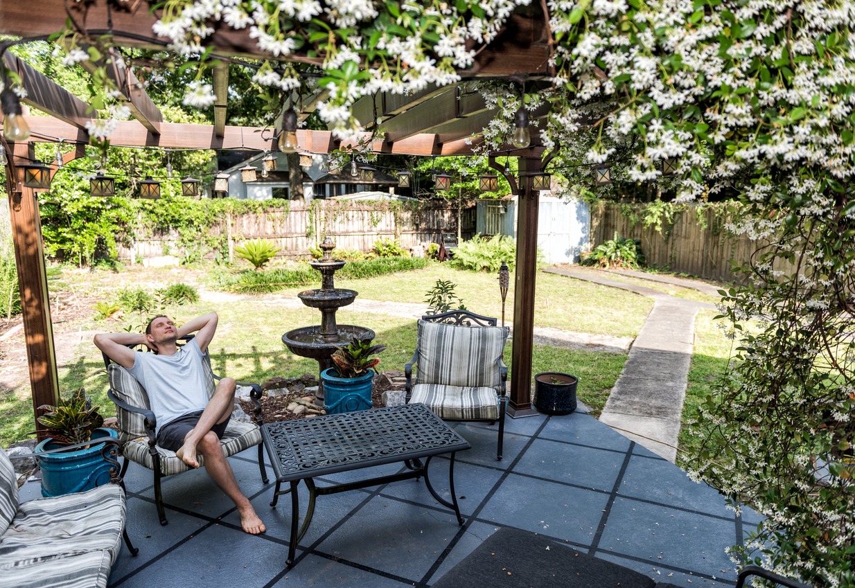A man relaxing under a pergola by a standalone fountain.