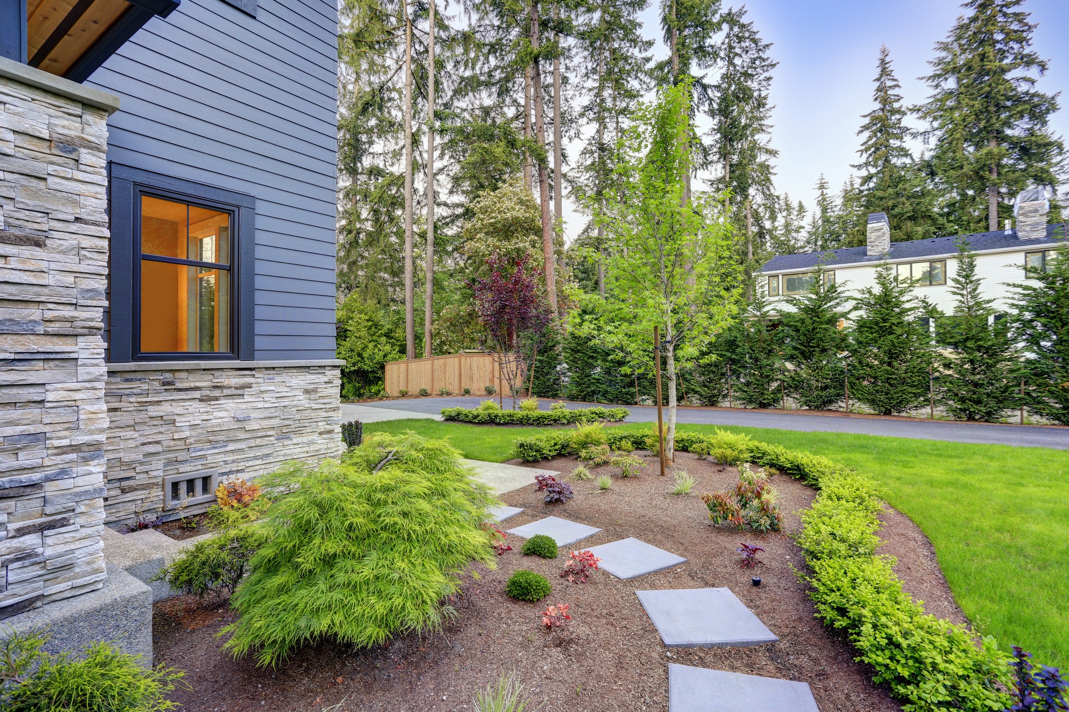 Exterior of grey two-story mixed siding home. View of a gravel path leading to the backyard and green grass in the garden.