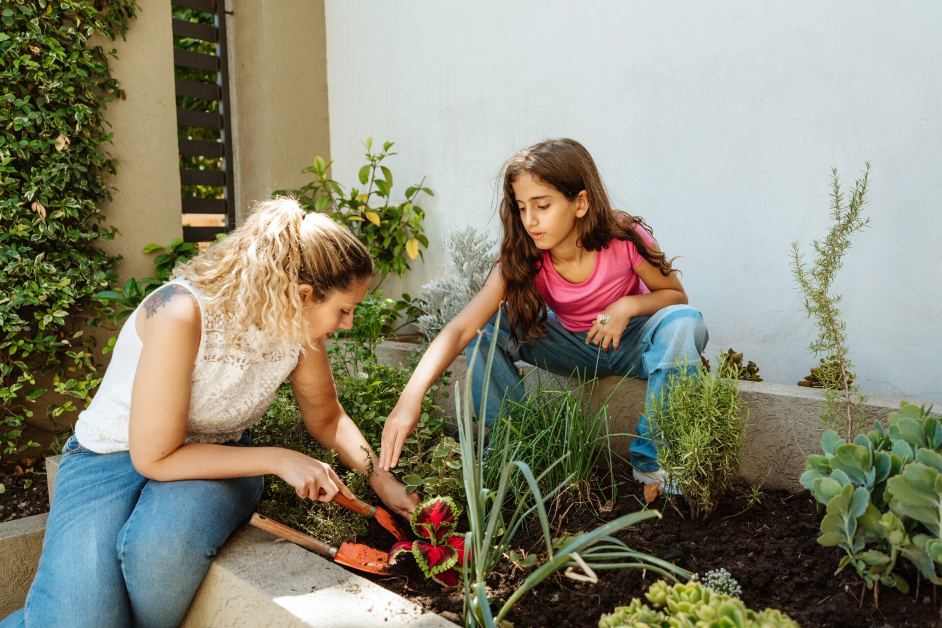 A mother and daughter bonding while gardening together in their backyard. They are planting and nurturing plants in a garden bed.