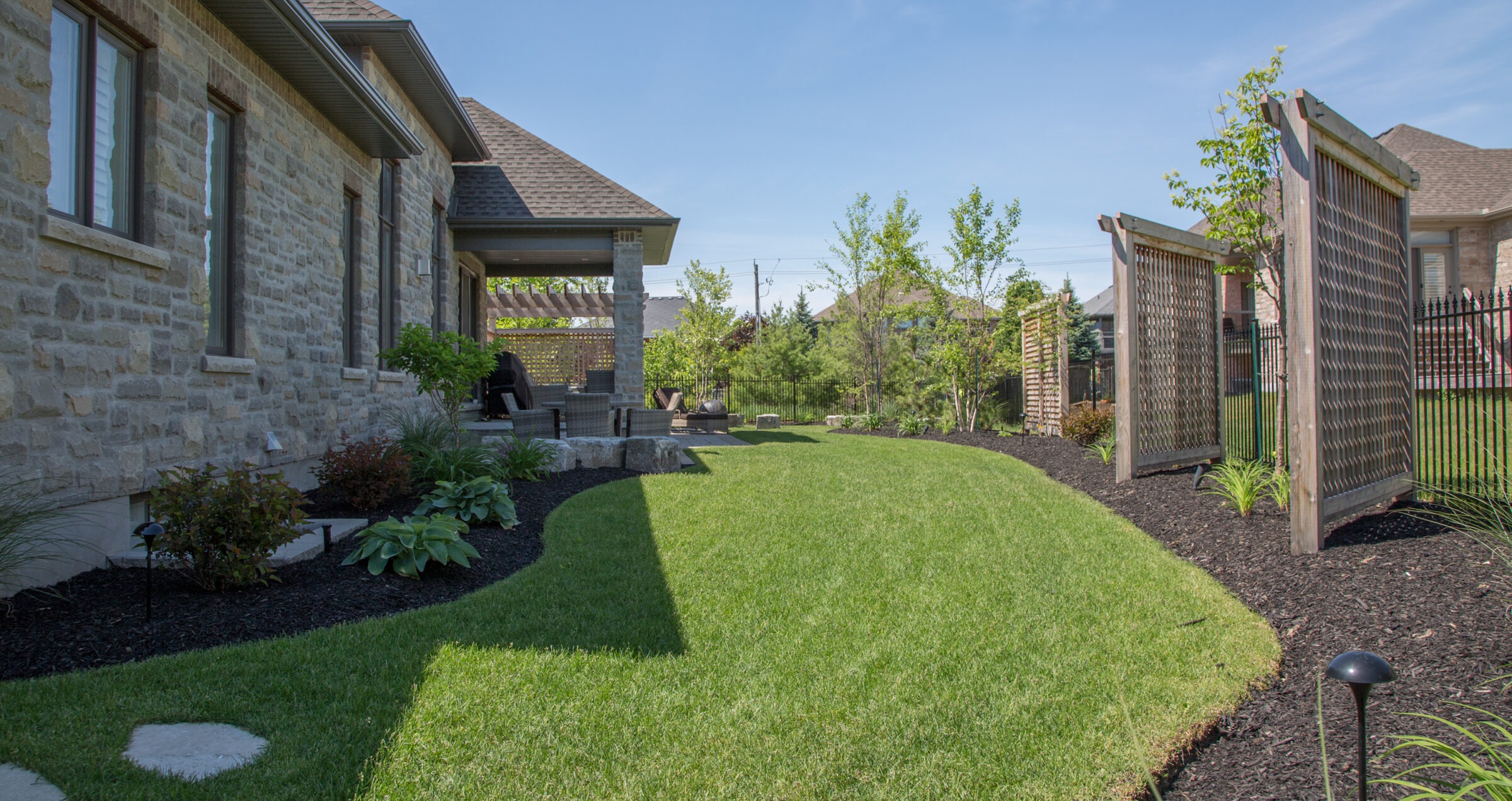 Well-manicured backyard featuring a lush green lawn, mulched garden beds, and wooden lattice