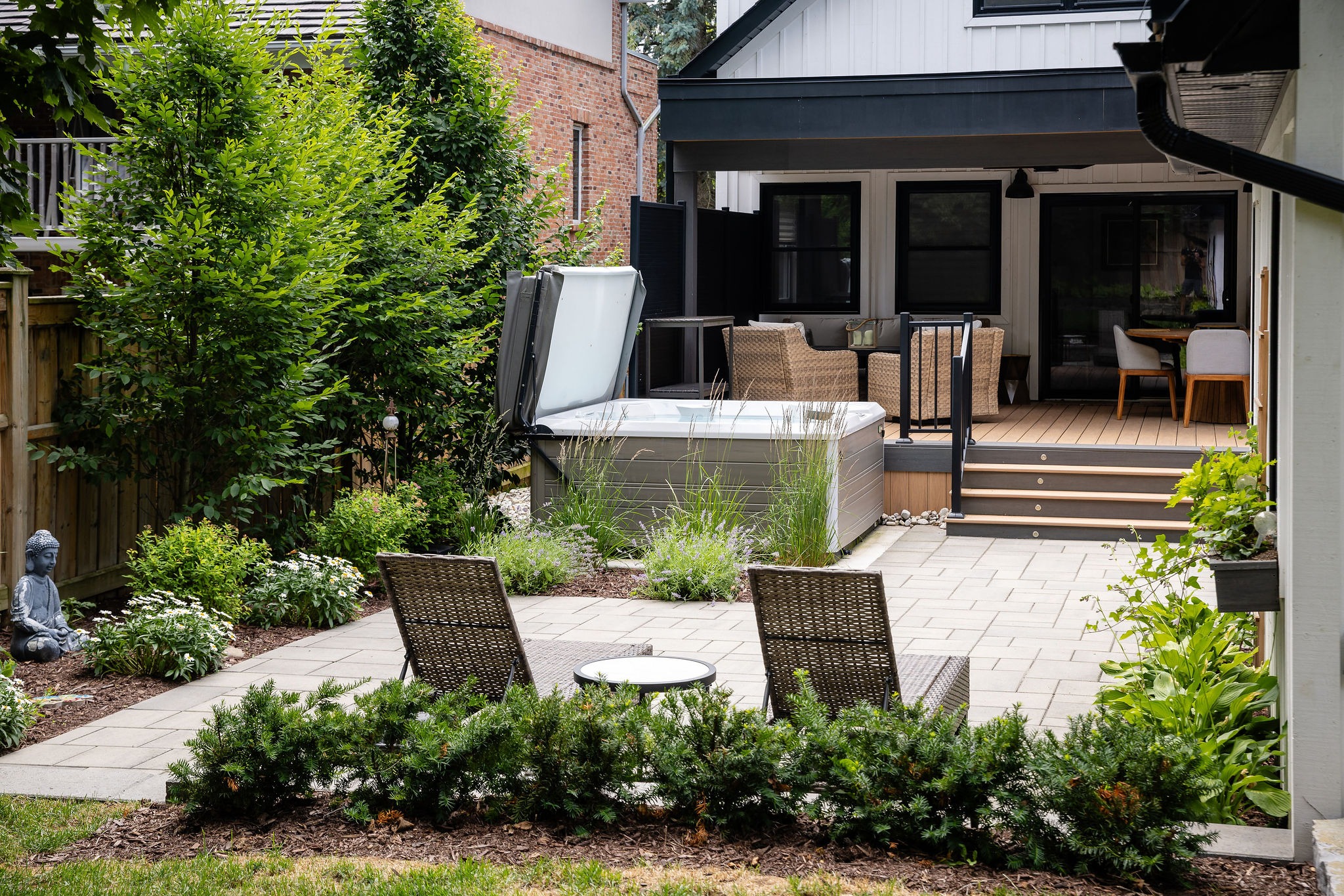 Private backyard patio with a hot tub, wicker lounge chairs, and lush plantings creating a cozy outdoor living space.