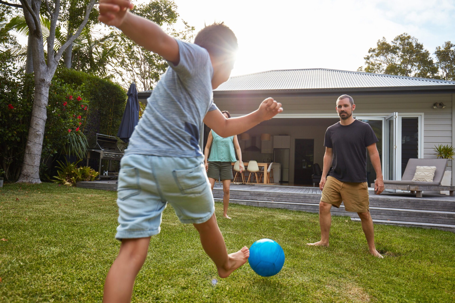A young boy kicking a ball towards his father as they play in the grass of their backyard.
