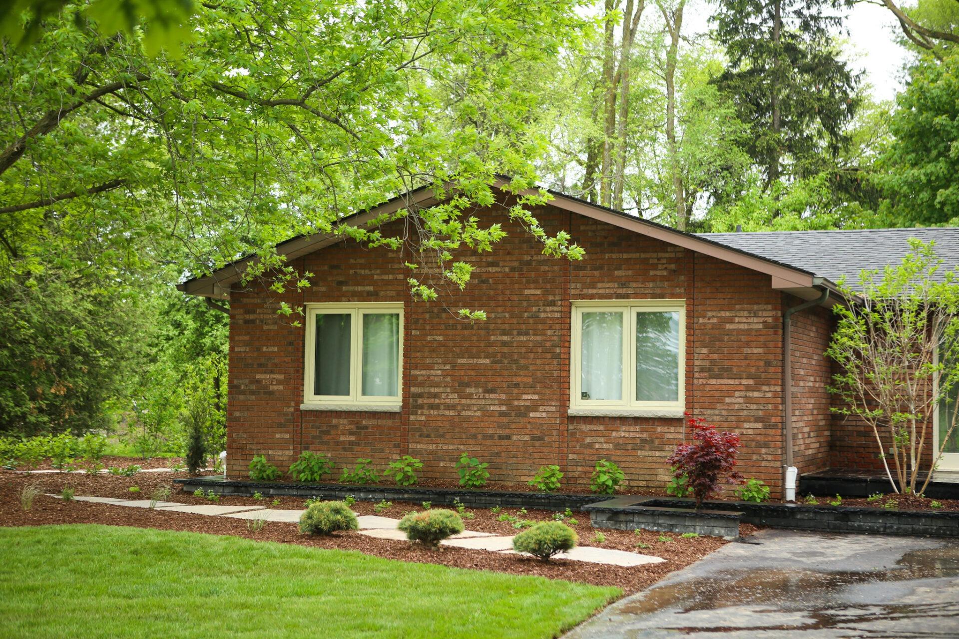 Front yard of a brick home with a mulched garden bed featuring young shrubs and a stone walkway bordered by lawn.