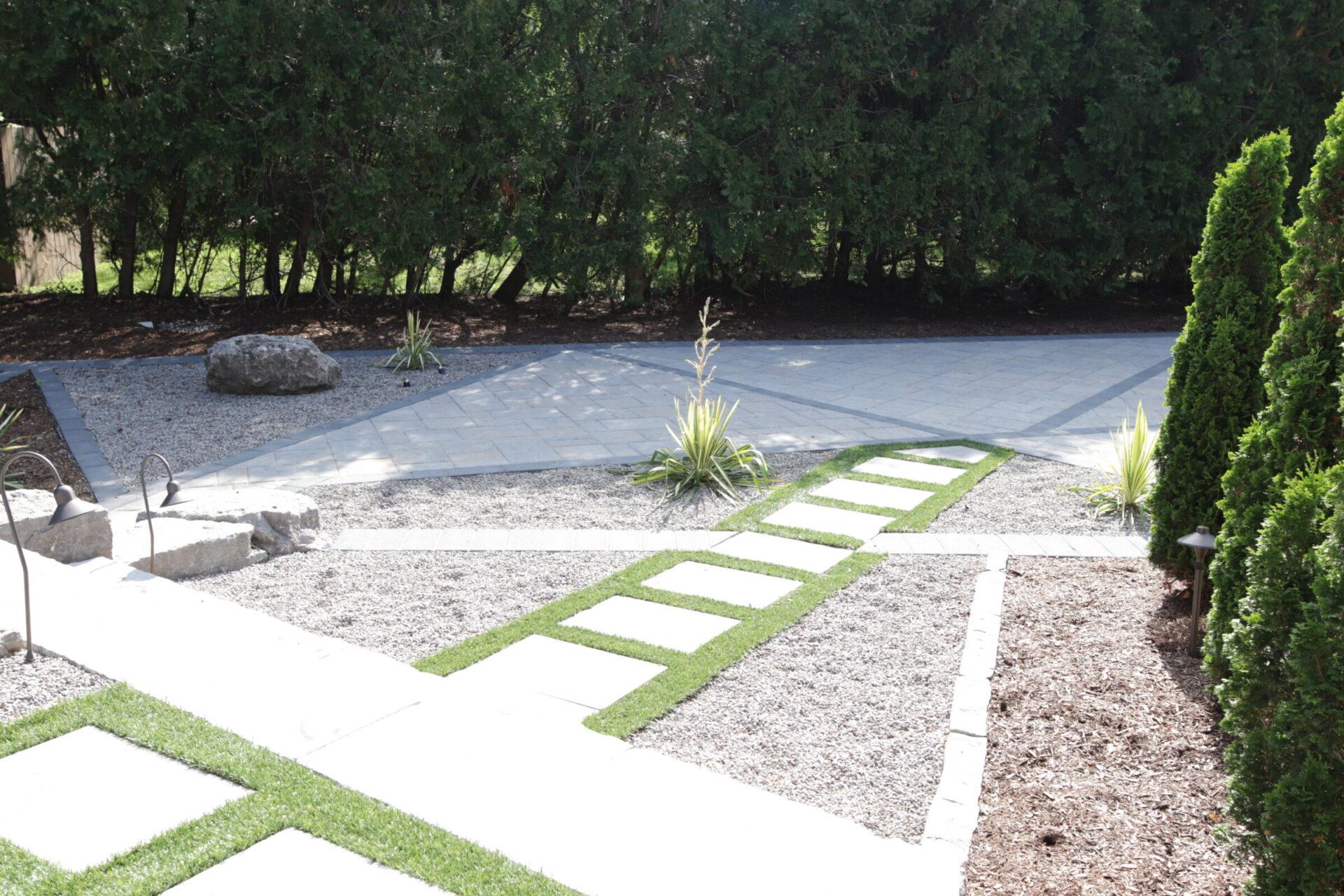 Geometric garden design with paver paths, gravel sections, and grass insets surrounded by young plants and evergreens.