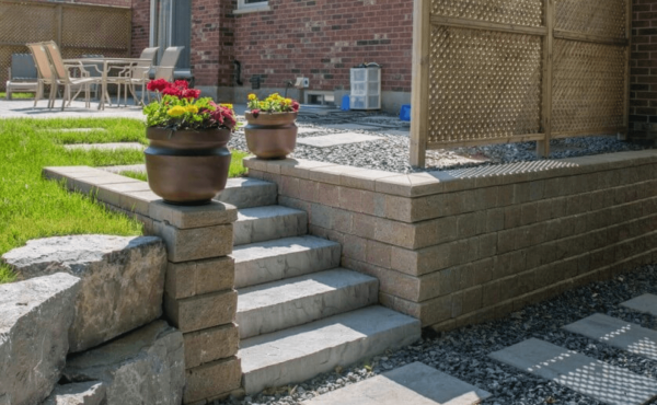 A photo of a stone walkway, stairway, and retaining wall. There is a privacy screen made of wood on the upper level.